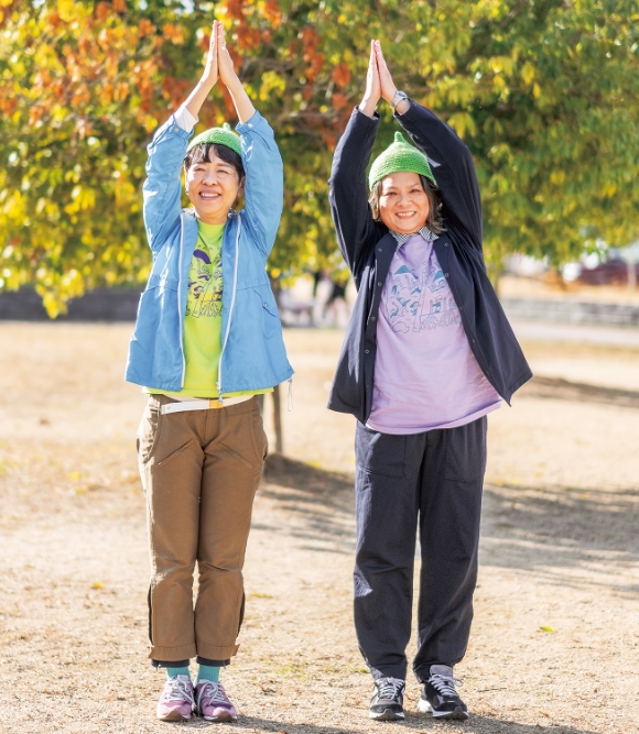 スタッフ用のアスパラ帽子をかぶり、2025年のイベントTシャツを着て、アスパラポーズをきめる國見さん（左）と末澤さん（右）