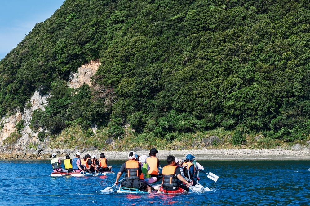 「いかだ集会」は、1チーム8人が力を合わせて、一周2kmの巴理島を手づくりのいかだでぐるりと一周し、速さを競い合う