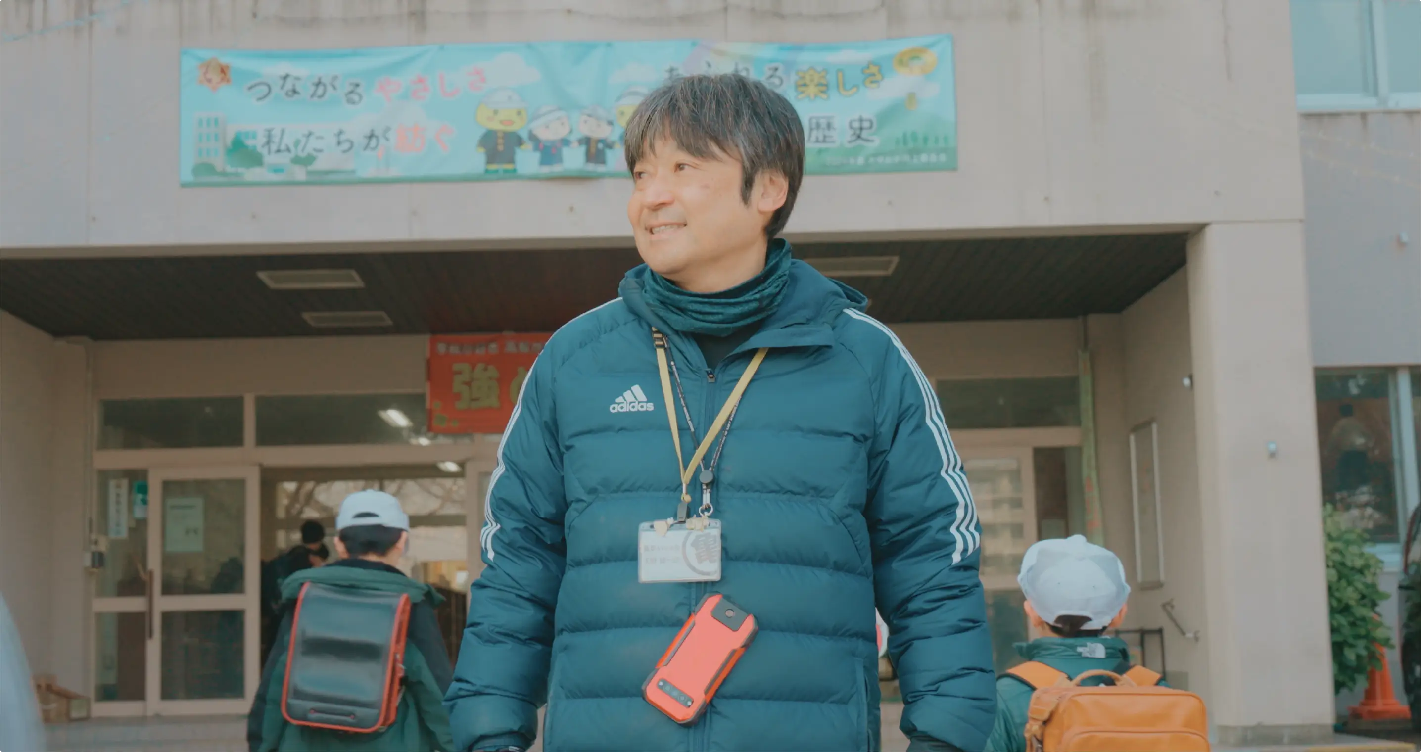 土木建築部　天野雄一朗さんの小学校の校門に立ち、あいさつ運動する写真